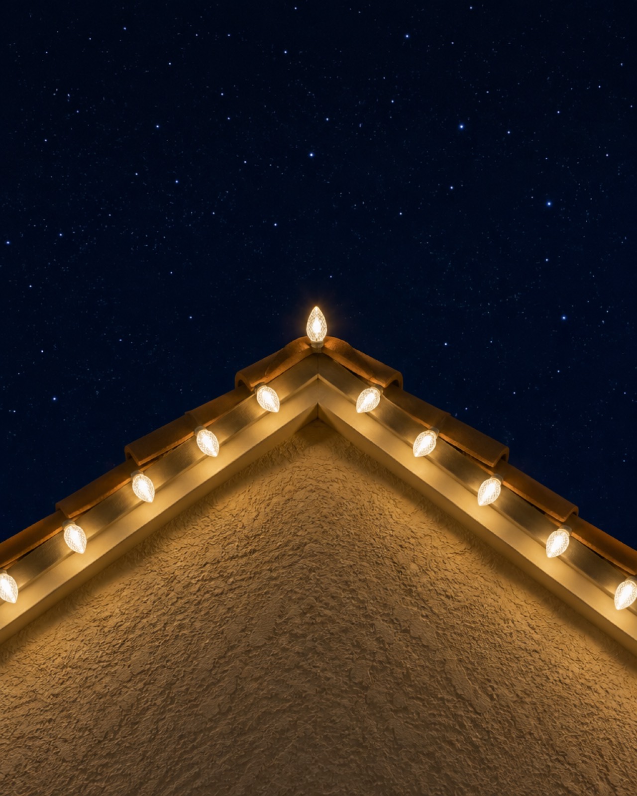 Close-up of warm-white C9 bulbs outlining a gable peak, the roofline look